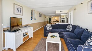 A living room with a TV, white entertainment unit, dark blue sofa, and a small white coffee table. - Summer Beach 608 by Seaside Vacations & Sales (Ocean City)