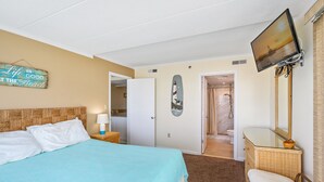 A hotel room with a bed, a television, a bathroom with a shower, and a door leading to another room. - Summer Beach 608 by Seaside Vacations & Sales (Ocean City)