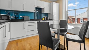 Een moderne keuken met witte kastjes, een zwart aanrecht en een eethoek met zwarte stoelen en een glazen tafel.