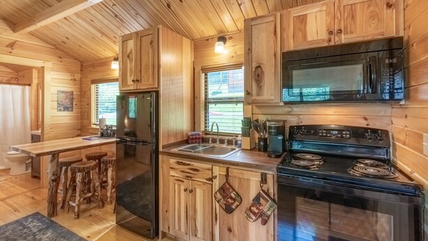 A wooden cabin-style kitchen with a refrigerator, stove, microwave, and wooden stools.