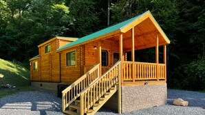 A two-story log cabin with a stone foundation, a wooden porch, and a staircase leading to the upper level. - Dogwood Cabin Unit 4-Wifi - Fire Pit - Mountain View & Stream (Bryson City)