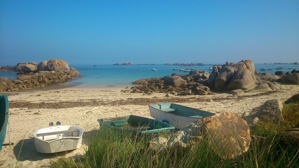 Una playa con barcos, rocas y agua azul cristalina.