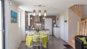 Cocina moderna con una isla central, iluminación colgante y un comedor con una mesa dispuesta para dos.