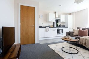 A modern living room with a flat-screen TV, a sofa, a coffee table, and a kitchen in the background.