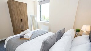 Et hotelværelse med seng, et klædeskab, et vindue og et sengebord med lampe.