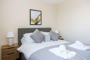 A hotel room with a bed, pillows, a nightstand with a lamp, and a framed picture on the wall.