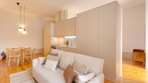 Una sala de estar moderna con un sofá, una mesa de comedor con sillas, una zona de cocina y un taburete de madera.