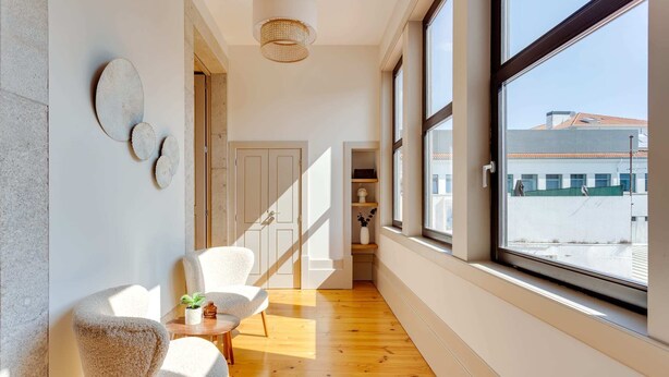 Un pasillo amplio con piso de madera, una puerta blanca y un ventanal con vistas a edificios.