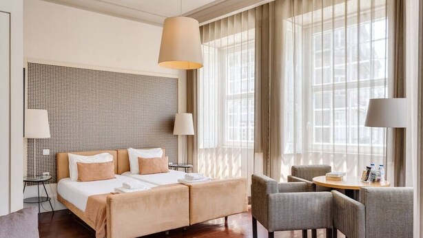A hotel room with a large bed, two bedside tables, a desk with chairs, and a large window with curtains. - Traça Apartments by DA'HOME - Studio Deluxe #1 (Porto)