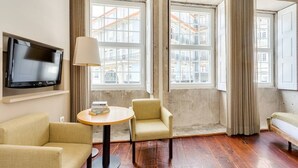 A hotel room with a TV, two armchairs, a round table, and large windows with curtains. - Traça Apartments by DA'HOME - Studio #2 (Porto)