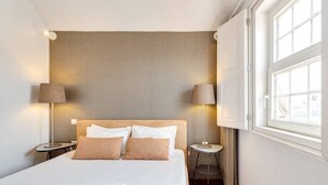 Ein Hotelzimmer mit einem großen Bett, zwei Nachttischen, zwei Lampen und einem Fenster mit Vorhängen.
