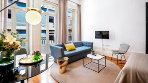 A modern living room with a blue sofa, a round coffee table, a TV mounted on the wall, and a dining table with a vase of flowers. - The A5 Luxury Studio #1 by DA'HOME (Porto)