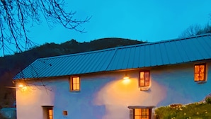 A two-story house with a stone foundation, a metal roof, and a small front porch.
