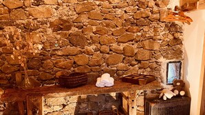 A rustic stone wall with a wooden bench, baskets, and a bear figurine.
