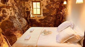 A rustic stone room with a bed, a small window, and a wooden ceiling.