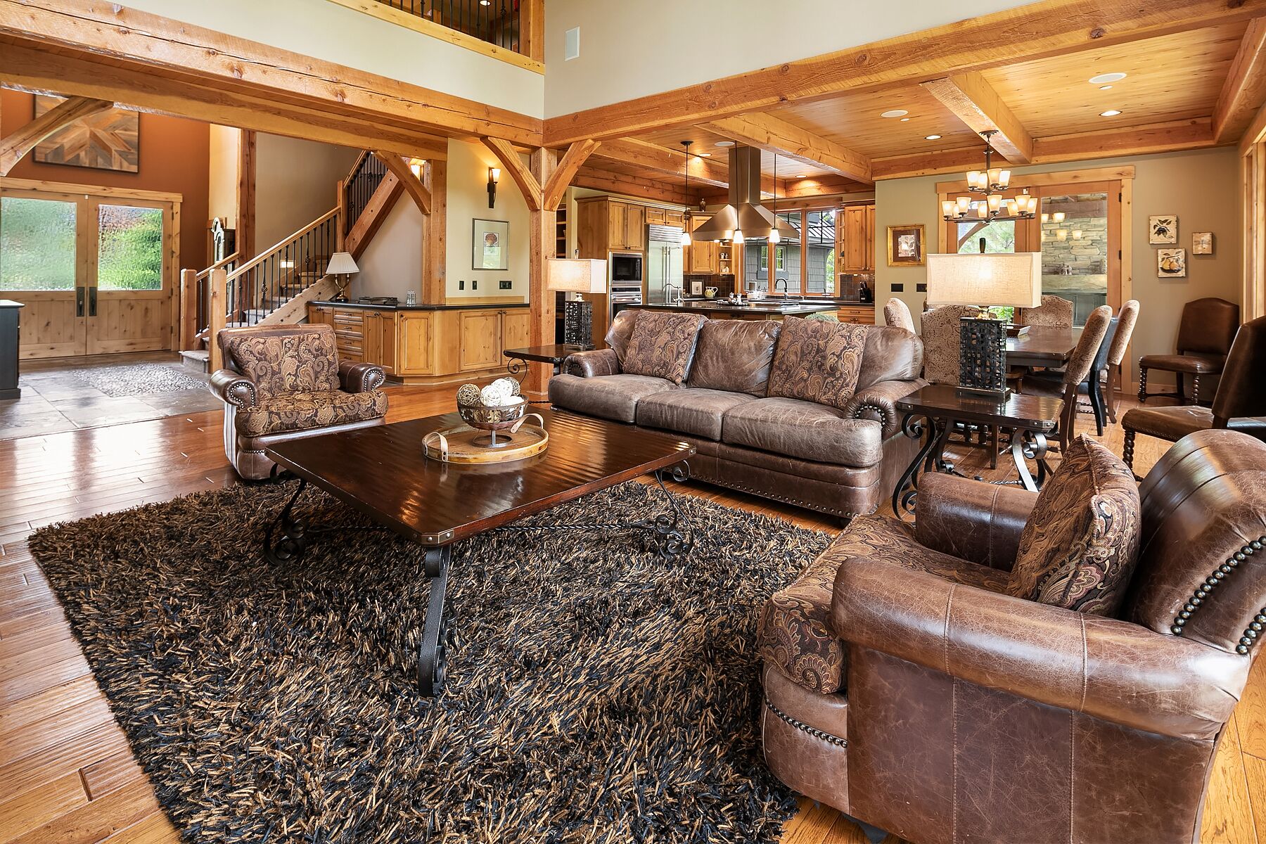 A spacious living room with a large wooden ceiling, a fireplace, and a dining area with a dark wooden table and leather chairs.