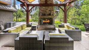 Une terrasse extérieure dotée de meubles en osier, d’une cheminée en pierre et d’une structure en forme de pergola.