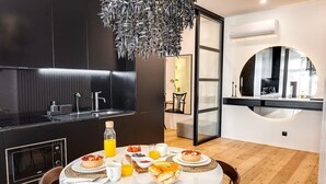 A modern kitchen with a dining area, featuring a round table with breakfast items, a built-in oven, and a unique ceiling light fixture.
