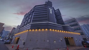 Un edificio moderno con un diseño angular distintivo, que presenta una entrada destacada con escalones iluminados y fachada de ladrillo.