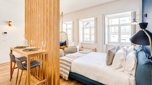 A modern bedroom with a wooden partition, a bed with white bedding, a blue headboard, and a desk with chairs. - Boavista Blue Studio by DA'HOME (Porto)
