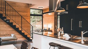 Une cuisine moderne dotée d’un îlot central, de meubles de couleur noire, d’appareils électroménagers en acier inoxydable et d’un escalier en bois.
