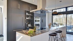 Une cuisine moderne dotée d’un îlot central, d’appareils électroménagers en acier inoxydable et d’une grande fenêtre offrant une vue sur l’extérieur.