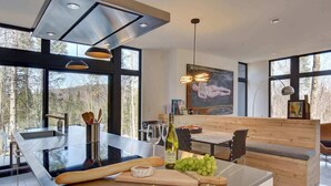 Une cuisine moderne dotée d’un îlot central, de grandes fenêtres et d’un coin repas avec un banc en bois.