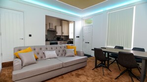 Un salon moderne avec un canapé beige, une table à manger avec des chaises, et une cuisine en arrière-plan.
