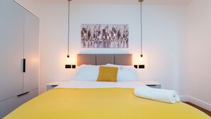 Une chambre d’hôtel moderne avec un grand lit, un tableau représentant un paysage urbain au-dessus du lit et deux lampes de chevet.