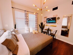 Um quarto com uma cama, uma escrivaninha, uma cadeira, um espelho e uma televisão fixada na parede.