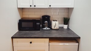 A kitchen with white cabinets, a microwave, a coffee maker, a toaster, and a potted plant. - Nine20 Collins (Miami Beach)