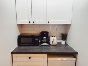 Eine Küche mit weißen Schränken, einer Mikrowelle, einer Kaffeemaschine, einem Toaster und einer Topfpflanze.