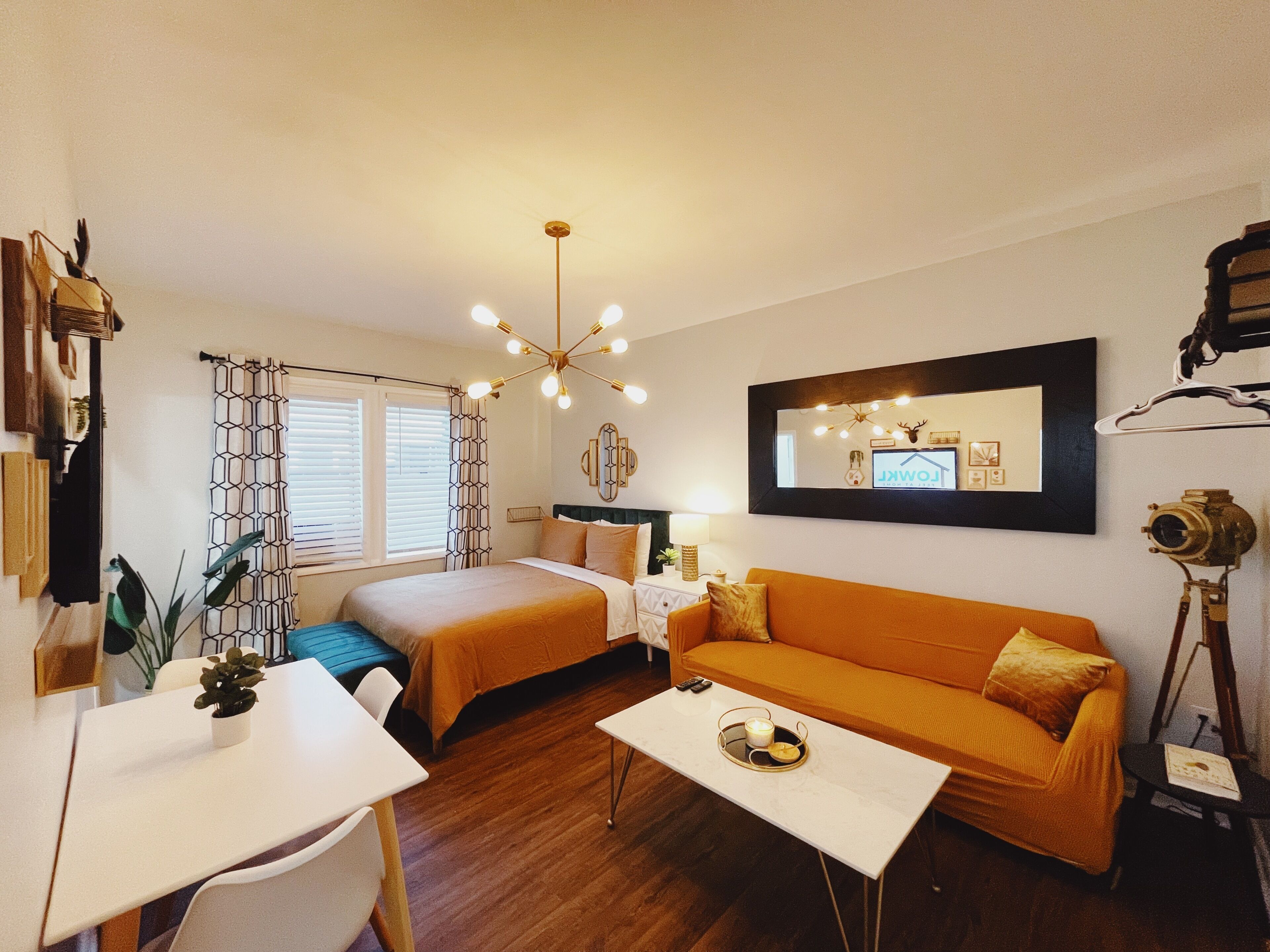 Ein gut beleuchteter Raum mit einem Bett, einem Schlafsofa, einem Schreibtisch und einem Spiegel an der Wand.