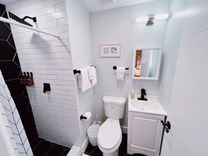 Un bany amb vàter blanc, un lavabo, un mirall i una zona de dutxa.