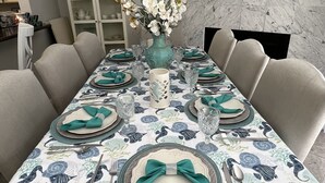 Une table à manger dressée avec une nappe à motifs floraux, un vase rempli de fleurs et un tableau encadré accroché au mur.