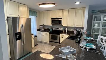 A modern kitchen with stainless steel appliances, white cabinetry, and a dining area with a glass table and chairs.