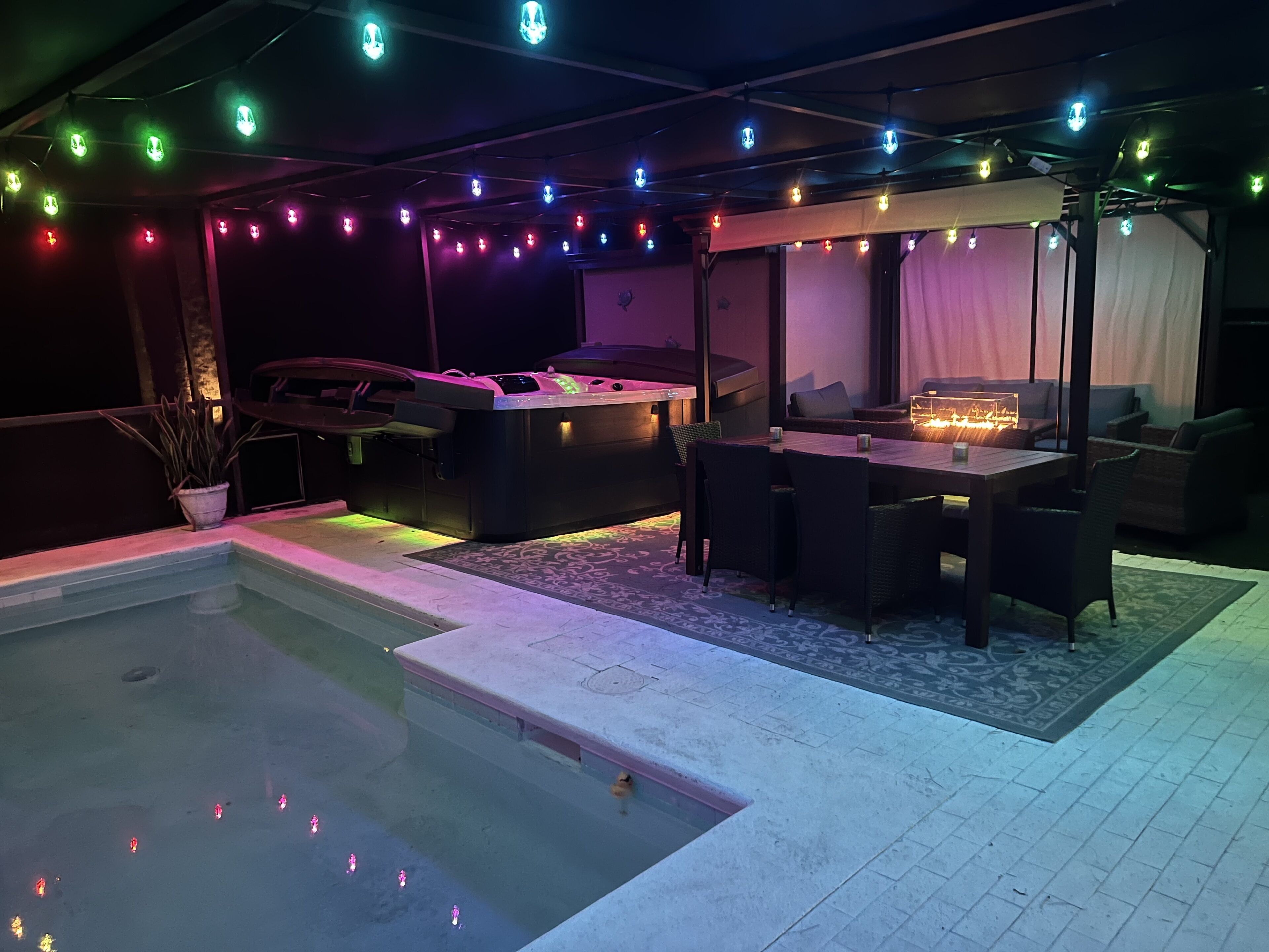 A pool area with a hot tub, seating, and string lights.