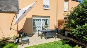 A patio with a table and chairs, a white umbrella, and a potted plant.