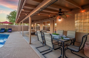 An outdoor patio with a pool, covered seating, and a dining area.