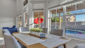A modern dining area with a wooden table, grey upholstered chairs, and large windows offering a view of the outdoors. - Recently renovated Phoenix home with private heated pool and mountian veiws  (Phoenix)