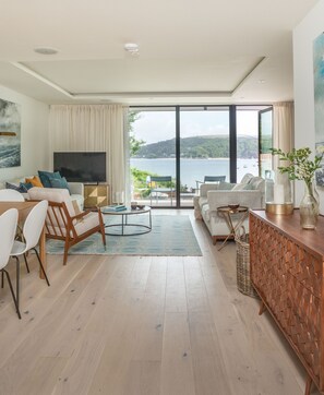 A modern living room with a large TV, comfortable seating, a dining area, and a view of the sea. - Luxury beachfront property sleeps 6 - parking (Salcombe)