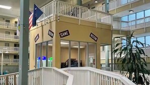 A multi-level hotel atrium with a central staircase, balconies, and signs indicating 'GAME ROOM' and 'ROOM' areas.