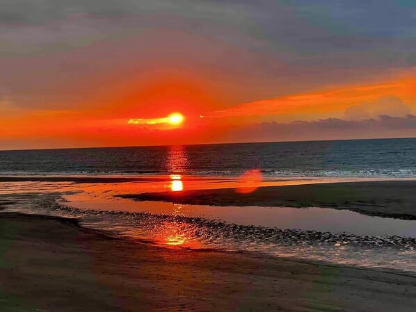 A sunset over a beach with calm waters reflecting the sky.