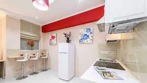 A modern kitchen with white appliances, a red accent wall, and a bar area with stools. - Orange 2: Studio Apartment in St. Julian's (Swieqi)