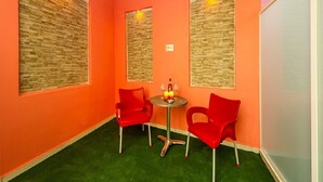 A room with two red chairs, a small round table with a bottle and glasses, and a wall with a textured panel. - Orange 2: Studio Apartment in St. Julian's (Swieqi)