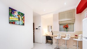 A modern kitchen with white cabinets, a dining area with white bar stools, and a painting on the wall. - Orange 2: Studio Apartment in St. Julian's (Swieqi)