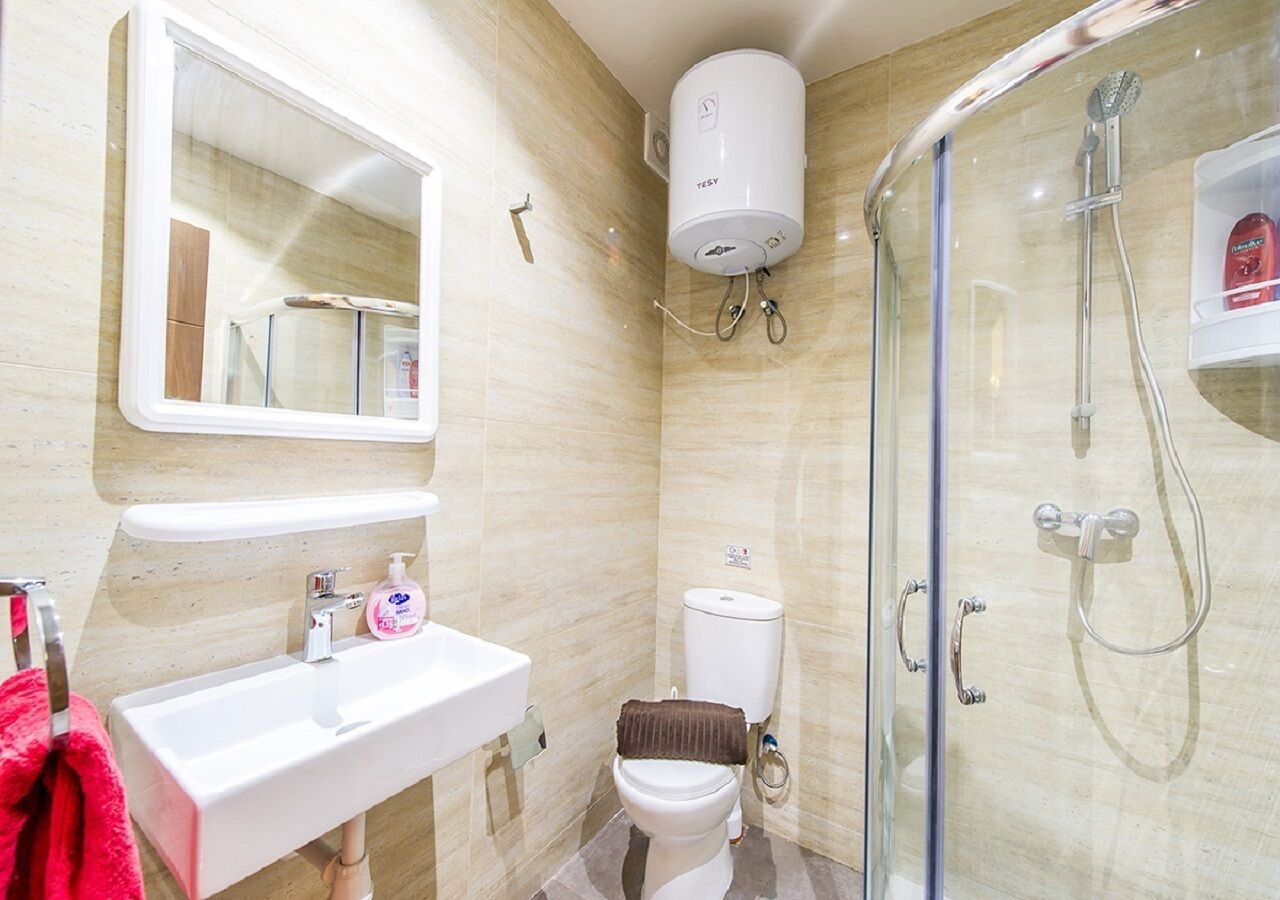 A bathroom with a white sink, mirror, toilet, and glass-enclosed shower.