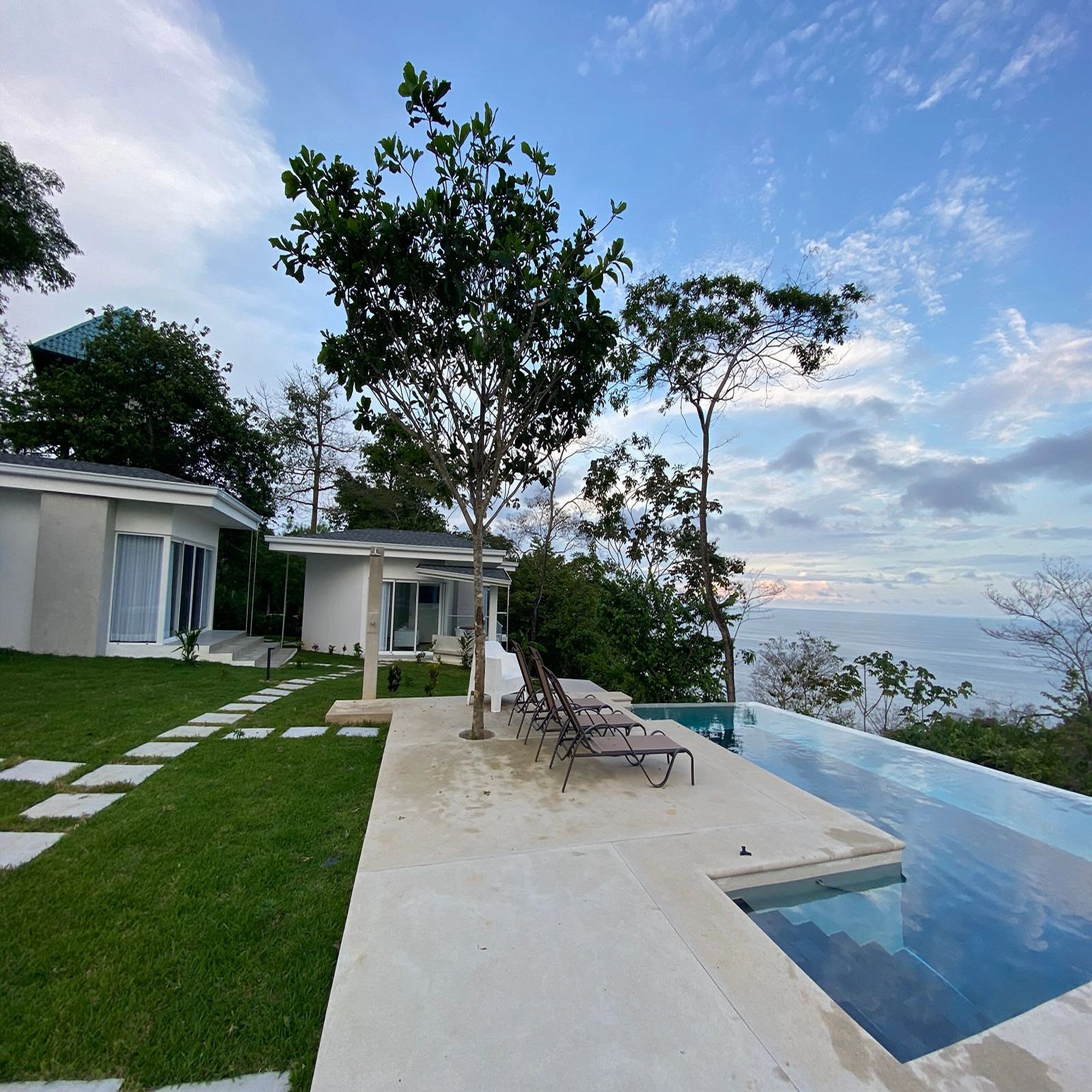 A modern house with a swimming pool, a lawn, and a view of the ocean.
