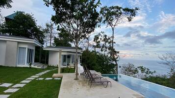 A modern house with a swimming pool, a lawn, and a view of the ocean.