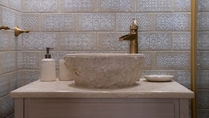 A bathroom with a marble sink, gold faucet, and patterned tiles.